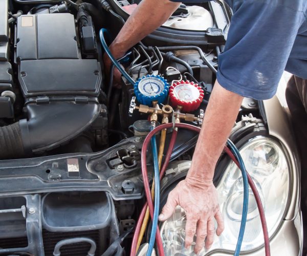 Mechanic with manometer inspecting auto vehicle air-condition co